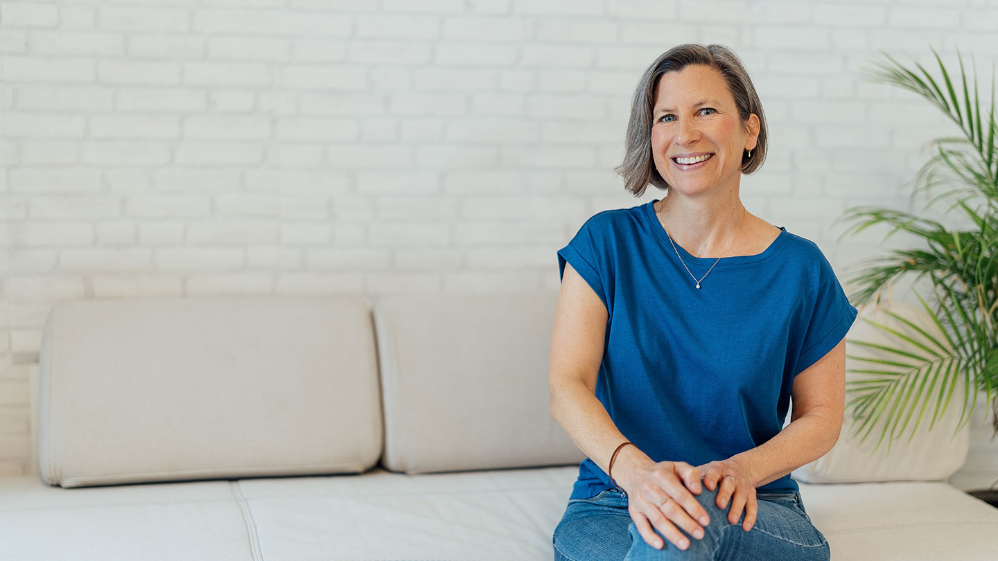 Eine Frau sitzt auf einer Couch und lächelt.